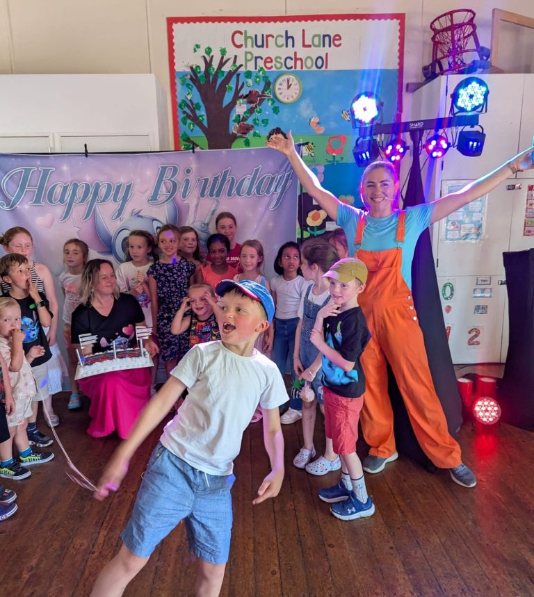 A performer in orange overalls entertains a group of children at a lively event.