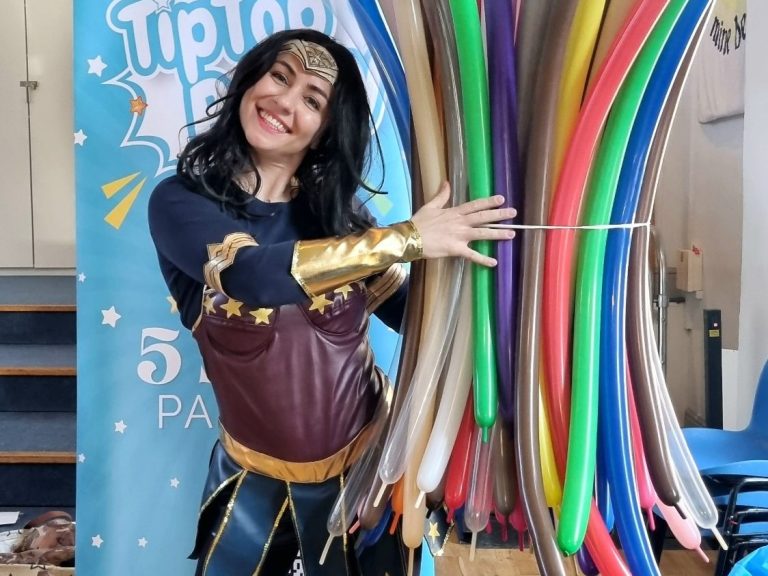 Superhero party entertainment with games, activities, and laughs. A person dressed as Wonder Woman holding a bundle of coloured balloons.